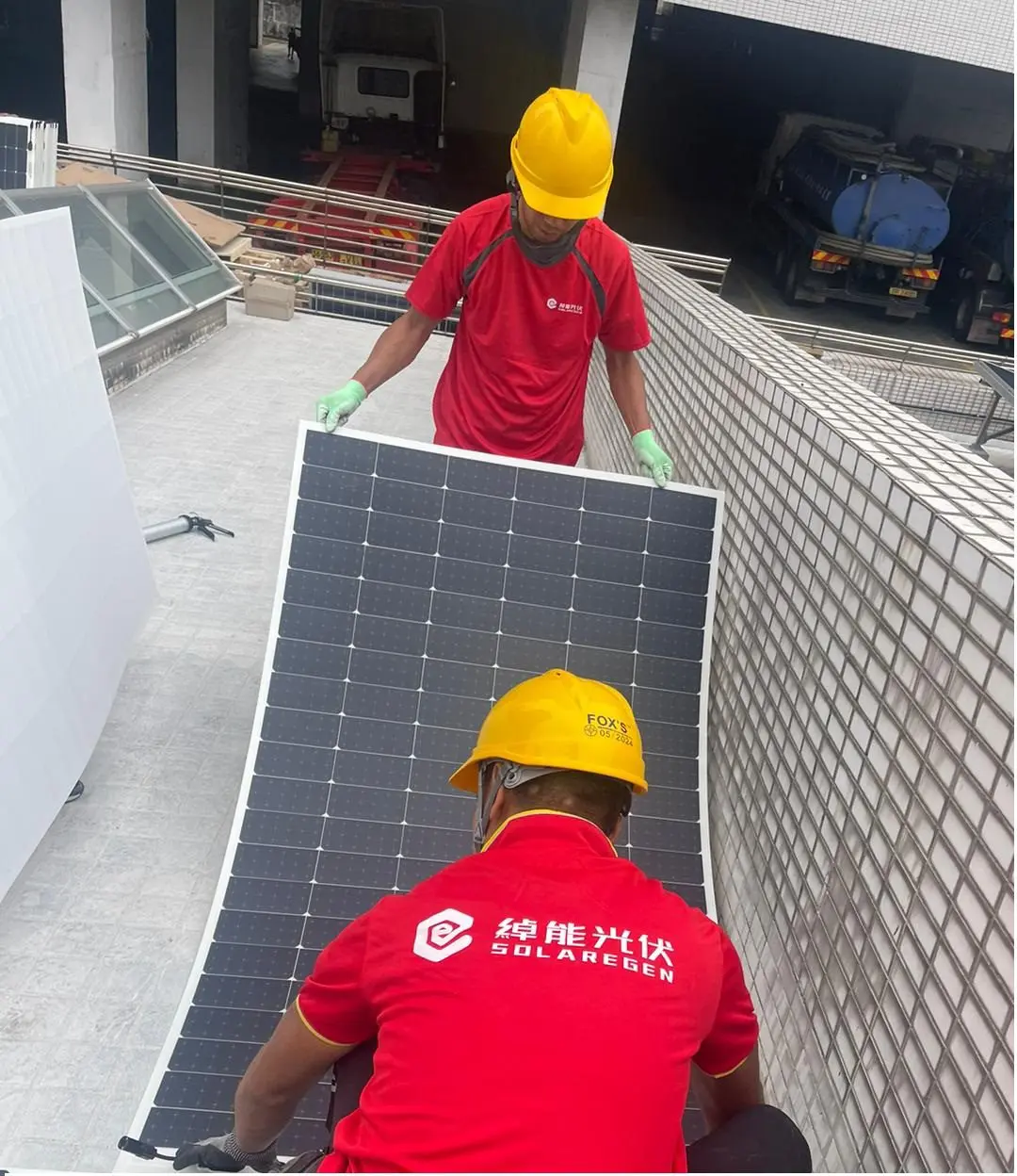 兩位穿紅色綽能光伏工作服及安全帽的人員搬運太陽能組件。